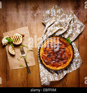 Torta di cipolle o tart servita con halfs grigliate di cipolla e erbe aromatiche fresche. Stile rustico. Foto Stock