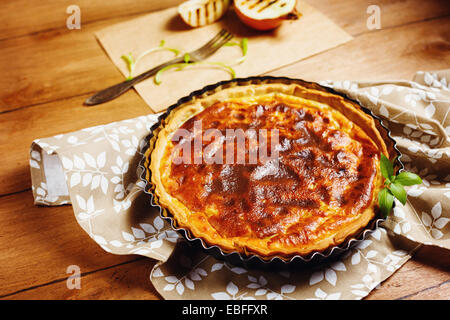 Torta di cipolle o tart servita con grigliate di metà della cipolla e erbe aromatiche fresche. Stile rustico. Vista ravvicinata. Immagine tonica in colori caldi. Foto Stock