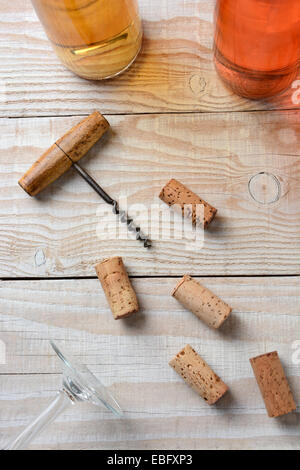 Verticale alto angolo primo piano di un vecchio cavatappi su una tabella con tappi casuale due bottiglie di vino e un bicchiere di vino inferiore. Foto Stock