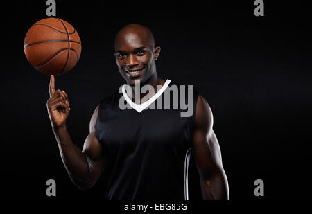 Ritratto di felice giovane africana atleta di pallacanestro di bilanciamento sul suo dito. Fiducioso del giocatore di basket su sfondo nero Foto Stock