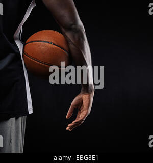 Close-up di una palla da basket in mano di un giovane atleta africana contro lo sfondo nero con copia spazio. Foto Stock