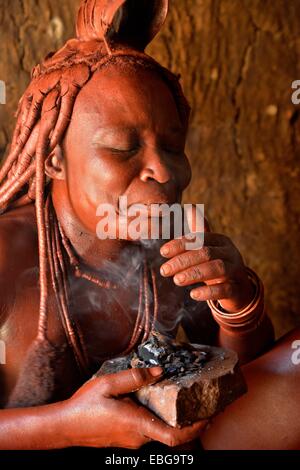 Tradizionalmente condita Himba donna nel suo rifugio, applicazione di profumo, Purros villaggio tradizionale, Purros, Kaokoland, Kunene, Namibia Foto Stock