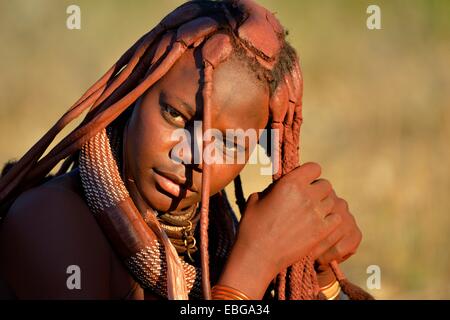 Giovane donna Himba facendo i suoi capelli, Ombombo, Kaokoland, Kunene, Namibia Foto Stock