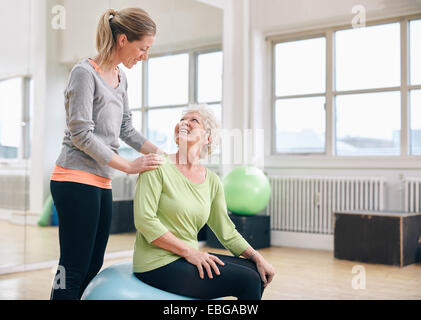 Femmina assiste istruttore senior donna che esercitano nel club salute. Donna anziana assistita da personal trainer presso la palestra. Foto Stock
