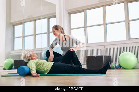 Senior donna avente una conversazione amichevole con il suo personal trainer mentre ti alleni in palestra. Il sambuco donna facendo pilates con palestra pullman. Foto Stock