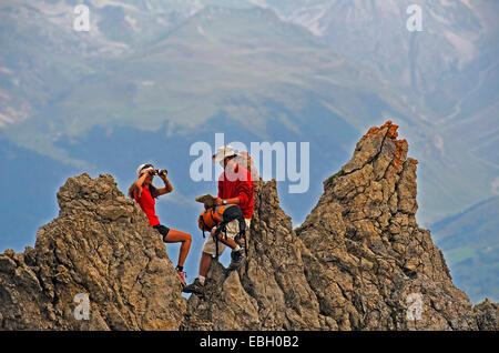 Due escursionisti seduti sulla parte superiore di una formazione di roccia e godendo della vista, Francia, Savoie, Parco Nazionale della Vanoise Foto Stock