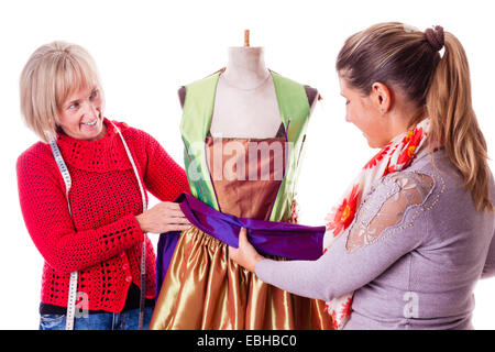 Due lieti seamstresses lavorando su un abito su un manichino isolate su uno sfondo bianco Foto Stock