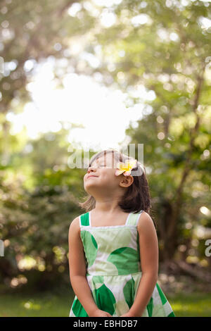 Giovane ragazza in giardino, indossando il fiore nei suoi capelli Foto Stock