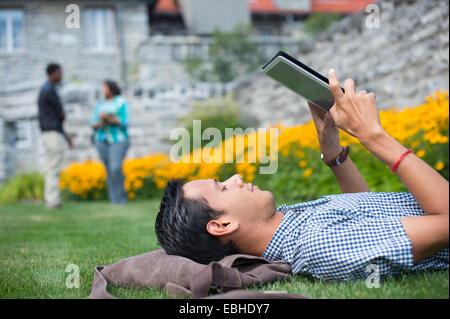 Studente maschio sdraiati sull'erba usando tavoletta digitale Foto Stock