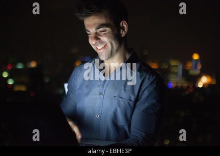 Giovane imprenditore digitando sulla tastiera portatile nella parte anteriore del grattacielo Finestra di ufficio di notte, Shanghai, Cina Foto Stock