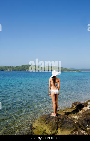 Vista posteriore della giovane donna che indossa un bikini guarda al mare, Milna, Brac, Croazia Foto Stock