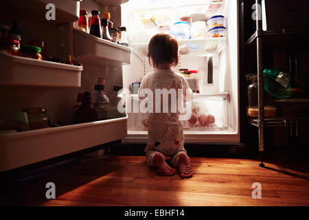 Vista posteriore del toddler maschio in ginocchio di fronte a aprire il frigo di notte Foto Stock