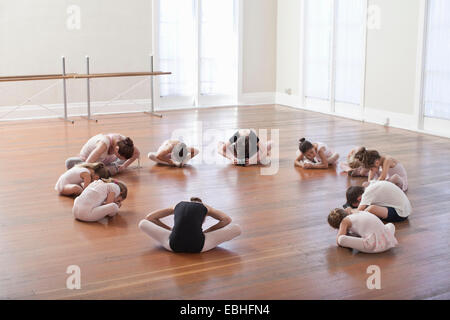 Bambini seduti sul pavimento la pratica di balletto con insegnante nella scuola di danza Foto Stock