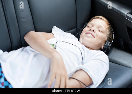 Ragazzo adolescente sorridente ascoltando le cuffie nel sedile posteriore della macchina Foto Stock