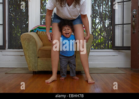 Bimbi maschio prendendo i primi passi con la madre in salotto Foto Stock