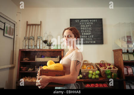 Ritratto di donna shop assistant il trasporto di frutta e verdura cassa nel paese store Foto Stock