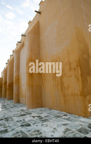 Vista laterale di Iglesia de chiesa del Gesù, che mostra solo il colore ocra adobe muro piastrellato in pietra marciapiede e cielo blu, Campeche, Messico. Foto Stock