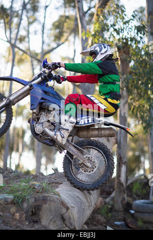 Giovane maschio motocross racer cavalcare fino oltre il log su pista forestale Foto Stock