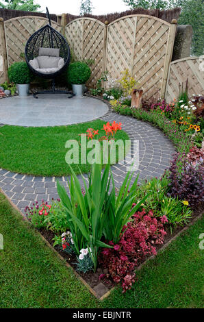 Un giardino design basato su curve che scorre intorno a un patio con appeso un sedia di canna Foto Stock