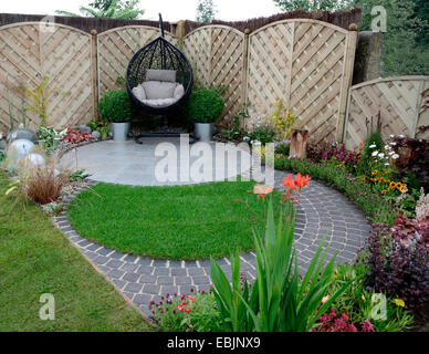 Un giardino design basato su curve che scorre intorno a un patio con appeso un sedia di canna Foto Stock