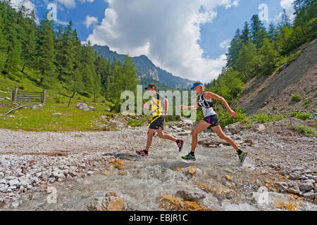 Coppia giovane che attraversa un ruscello saltando mentre trail running nei monti Dachstein, Austria, la Stiria, Dachstein Foto Stock