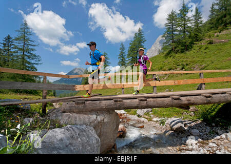 Coppia giovane in esecuzione su un ponte di legno su un ruscello mentre trail running nei monti Dachstein, Austria, la Stiria, Dachstein Foto Stock