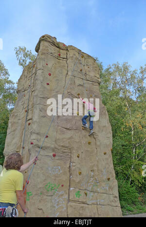 Little Boy di arrampicata in un professionista di parete di arrampicata cordata fino da un helper Foto Stock