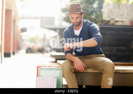 Metà uomo adulto seduto sul sedile, guardando a guardare, borse per lo shopping accanto a lui Foto Stock