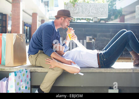 Metà adulto giovane rilassante sul sedile, bere drink, borse per lo shopping accanto a loro. Foto Stock