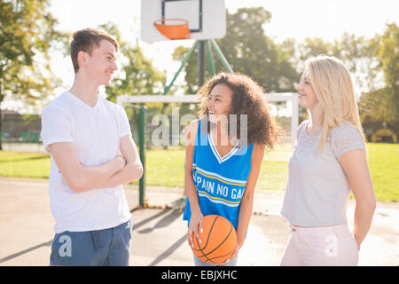 Tre adulti giovani giocatori di basket chat sul campo di pallacanestro Foto Stock