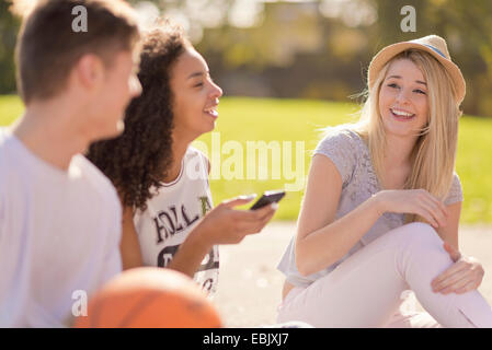 Tre adulti giovani giocatori di basket in chat e ridere Foto Stock