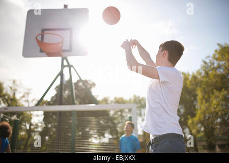 Maschio giovane giocatore di basket gettando la pallacanestro in hoop Foto Stock