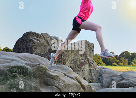 Collo in giù in vista della giovane femmina runner saltando su formazione di roccia Foto Stock