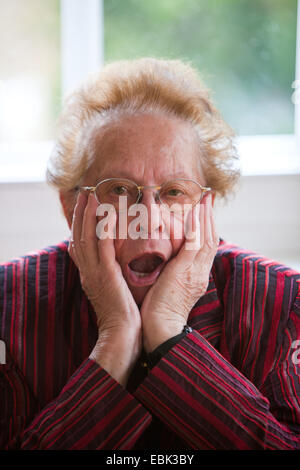 Vecchia donna siede a sbadigliare alla scrivania Foto Stock