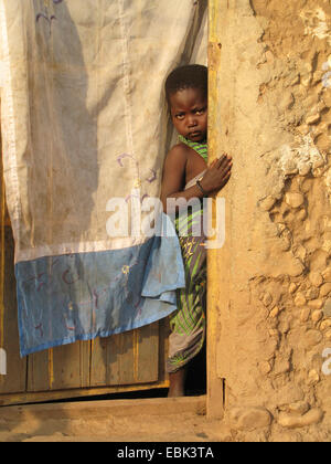 Bambina guardando fuori del di legno porta di ingresso di una semplice casa di fango in baraccopoli della capitale burundese Bujumbura mairie, Buyenzi Bujumbura Foto Stock