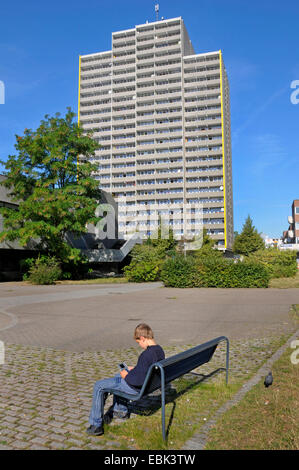 Ragazzo seduto sulla panca e riproduzione di gameboy, a torre in background, Germania, Chorweiler, Colonia Foto Stock