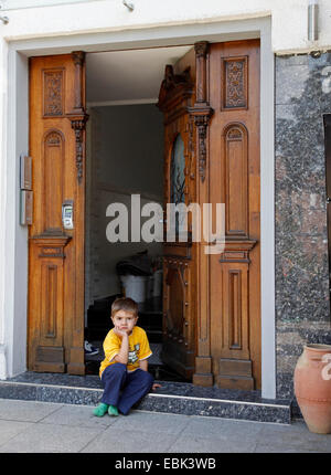Piccolo Ragazzo seduto di fronte ha aperto la porta di entrata Foto Stock