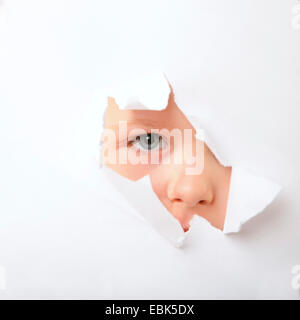 Little Boy il peering attraverso il foro in un libro bianco superficie con ome eye Foto Stock