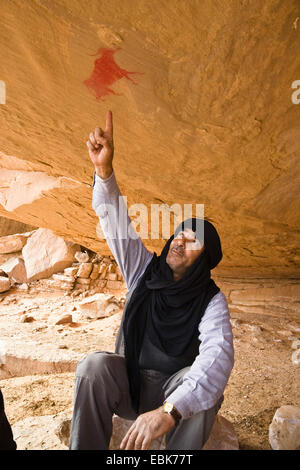 Touareg seduti sotto uno sperone di roccia puntando alla preistoria pitture rupestri presso l Acacus, Libia, Sahara Foto Stock