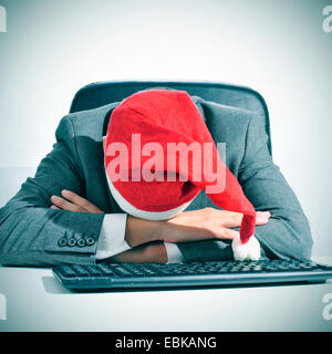 Un uomo in tuta con un cappello da Babbo Natale addormentato nella sua scrivania dopo un ufficio Christmas party Foto Stock