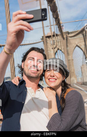 Stati Uniti d'America, nello Stato di New York, New York, Brooklyn, felice coppia tenendo selfie sul ponte di Brooklyn Foto Stock