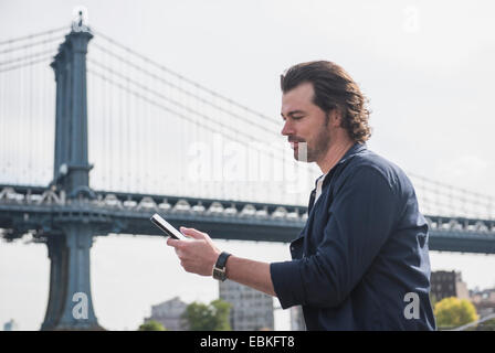 Stati Uniti d'America, nello Stato di New York, New York, Brooklyn, uomo utilizzando tablet pc, Manhattan Bridge in background Foto Stock