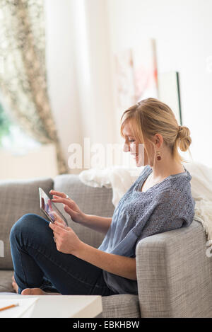 Donna sorridente seduto sul divano con il tablet pc Foto Stock