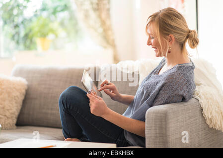 Donna seduta su un divano e utilizzando un tablet pc Foto Stock