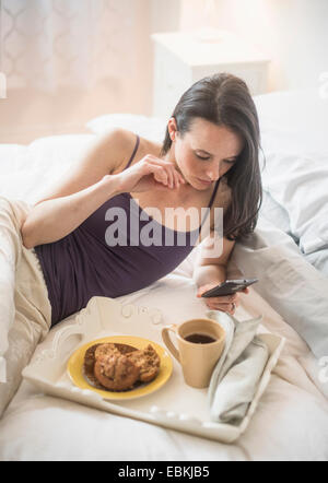 Donna con la colazione a letto, utilizzando il telefono cellulare Foto Stock