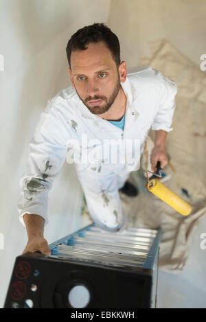 Uomo scaletta di arrampicata con rullo di vernice Foto Stock