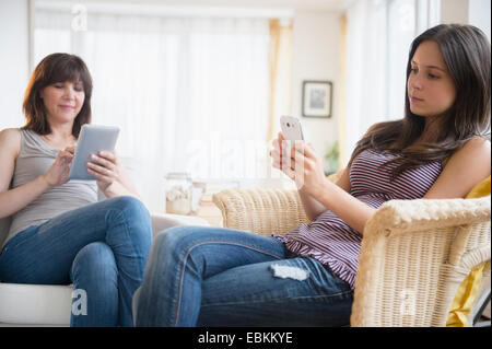 Ragazza adolescente (14-15) utilizzando smart phone e mom utilizzando digitale compressa in salotto Foto Stock