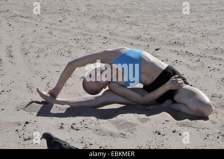 Bald donna esercizio yoga curvatura laterale o parivritta janu sirsasana, su di una spiaggia di sabbia Foto Stock