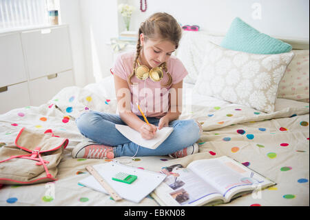 La ragazza (12-13) seduto sul letto facendo i compiti di scuola Foto Stock