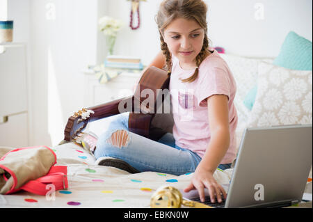 La ragazza (12-13) a suonare la chitarra e utilizzo di computer portatile Foto Stock